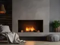 Nowoczesny kominek z palącym się ogniem, obudowany betonem. Inspiracja, jak obudować kominek, by stworzyć przytulną atmosferę.