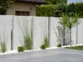 Nowoczesny betonowy płot z pionowymi elementami, ozdobiony trawami ozdobnymi i bukszpanami. Czy można postawić płot przy płocie? Tak, jeśli są tak stylowe!