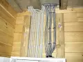 Instalacja elektryczna w domu drewnianym schemat: wiązki kabli w peszlach wychodzące z sufitu, przymocowane do drewnianych belek.