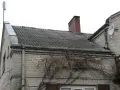 Dach pokryty eternitem, który zawiera azbest. Co to za materiał? Stary, szary eternit na dachu domu, z kominem i anteną satelitarną.