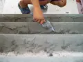 Ręka z kielnią wyrównuje betonowe schody wewnętrzne. To dobry sposób, czym wyrównać schody betonowe wewnętrzne.