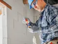 Elektryk w kasku i okularach montuje oprawkę żarówki. Ciekawe, ile za punkt elektryczny zapłacimy za taką pracę.
