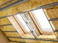 Ocieplenie dachu od wewnątrz: wełna mineralna między profilami stalowymi, widoczne okna dachowe w trakcie montażu.
