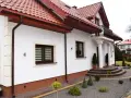 Biały dom z brązowym cokołem wokół, czerwonym dachem i ozdobnymi schodami.