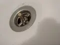 Metalowy korek do wanny z pokrętłem, widoczny mechanizm i włosy. Potrzebna naprawa.
