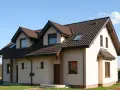 Nowy dom z piaskowy kolor elewacji, brązowym dachem i licznymi oknami.