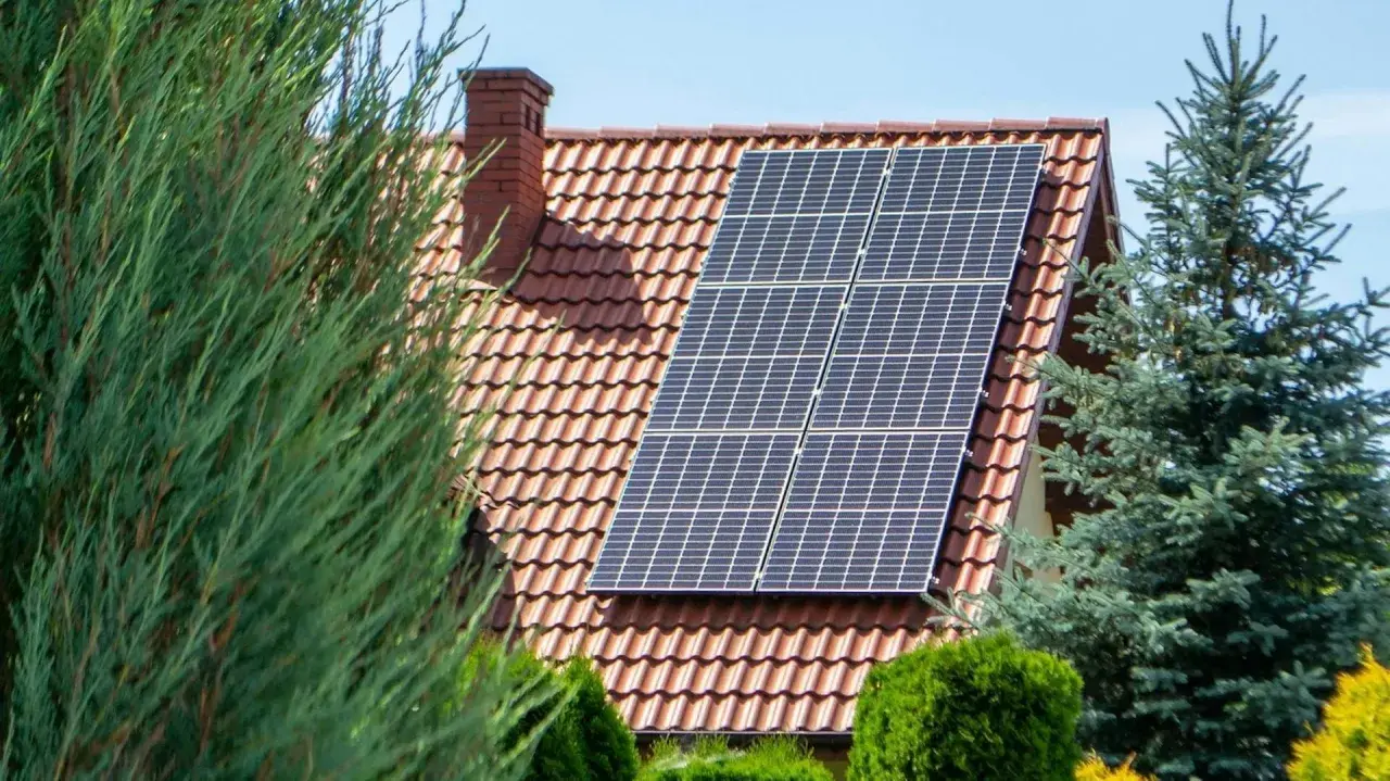Panele fotowoltaiczne na dachu domu, otoczone zielenią. Czy fotowoltaika się opłaca? To pytanie zadaje sobie wielu właścicieli domów.