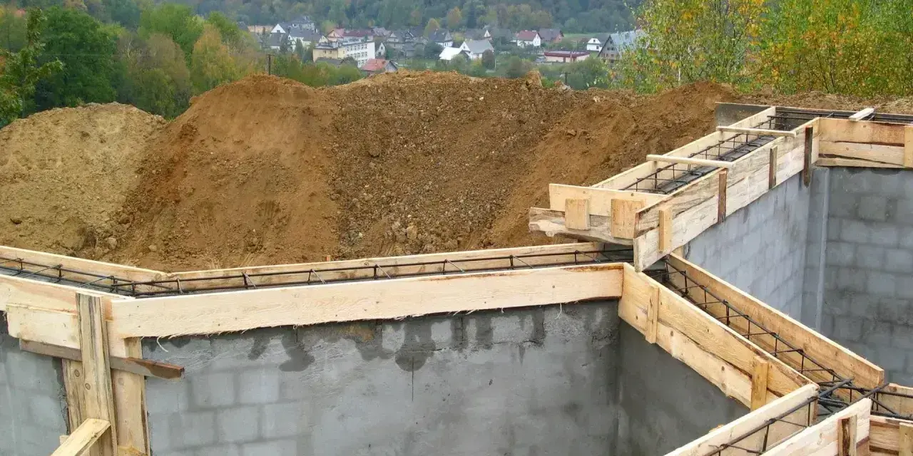 Budowa fundamentów zbrojonych, przygotowanie do wylania betonu. W tle widok na osiedle. To etap po uzyskaniu pozwolenia na budowę, zgodny z warunkami zabudowy.