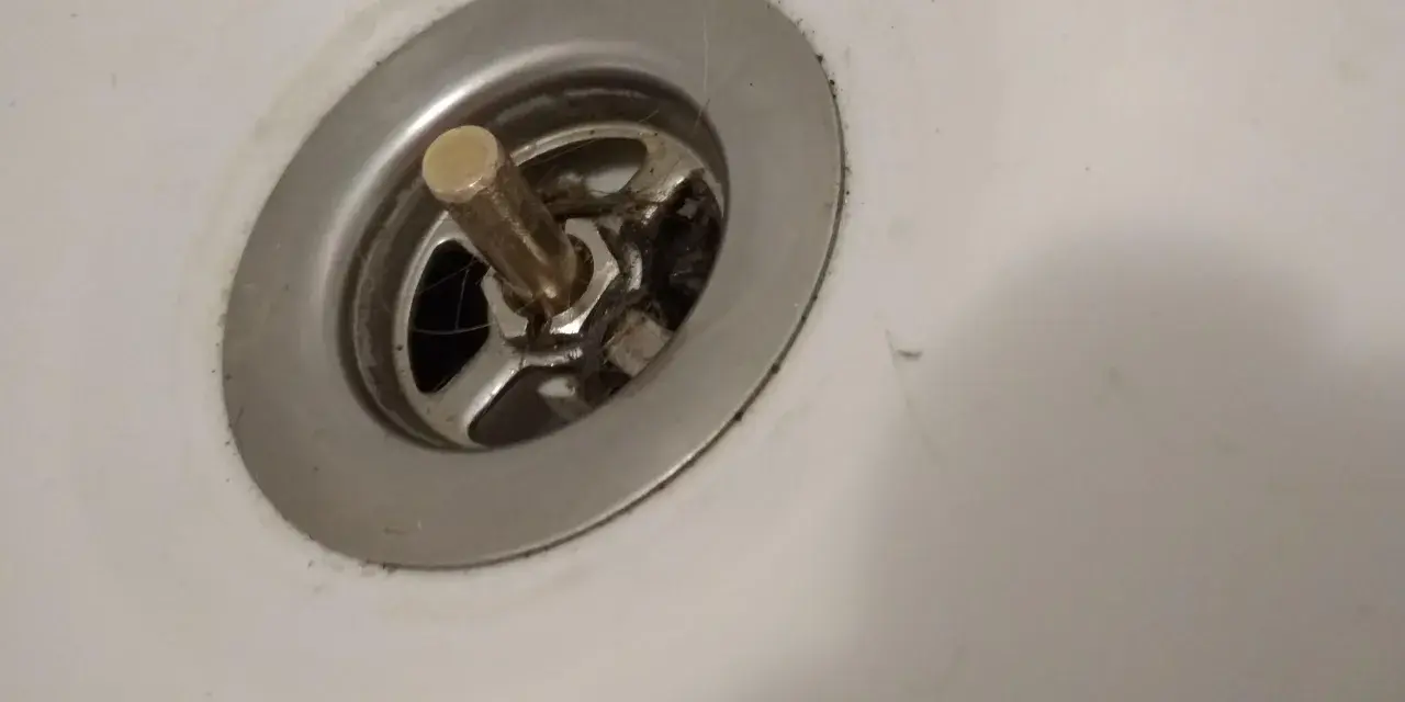 Metalowy korek do wanny z pokrętłem, widoczny mechanizm i włosy. Potrzebna naprawa.