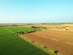 Rozległe, zielone i brązowe pola uprawne pod błękitnym niebem. W oddali widać maszyny budowlane, co może sugerować, ile trwa odrolnienie działki.