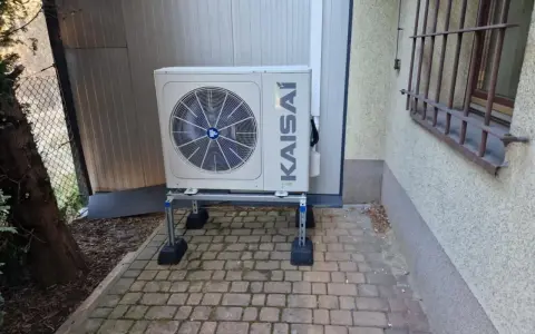 Jednostka zewnętrzna pompy ciepła KAISAI na metalowym stelażu, z widocznym wentylatorem. Optymalne taktowanie pompy ciepła zapewnia wydajność.