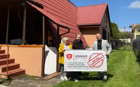 Trzy osoby trzymają baner "Budynek zalegalizowany", symbolizujący jak zrobić odbiór domu po 20 latach.