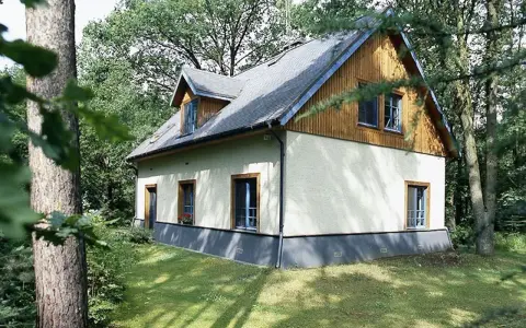 Dom otoczony zielenią, z widoczną odległością budynku od lasu. Drzewa tworzą naturalną barierę.