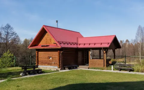 Drewniany domek letniskowy z czerwonym dachem, idealny na wypoczynek. Marzysz o takim? Sprawdź dofinansowanie na domek letniskowy!