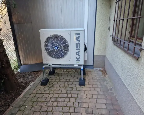 Jednostka zewnętrzna pompy ciepła KAISAI na metalowym stelażu, z widocznym wentylatorem. Optymalne taktowanie pompy ciepła zapewnia wydajność.