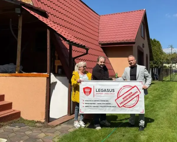 Trzy osoby trzymają baner "Budynek zalegalizowany", symbolizujący jak zrobić odbiór domu po 20 latach.
