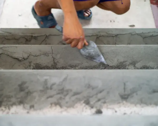 Ręka z kielnią wyrównuje betonowe schody wewnętrzne. To dobry sposób, czym wyrównać schody betonowe wewnętrzne.