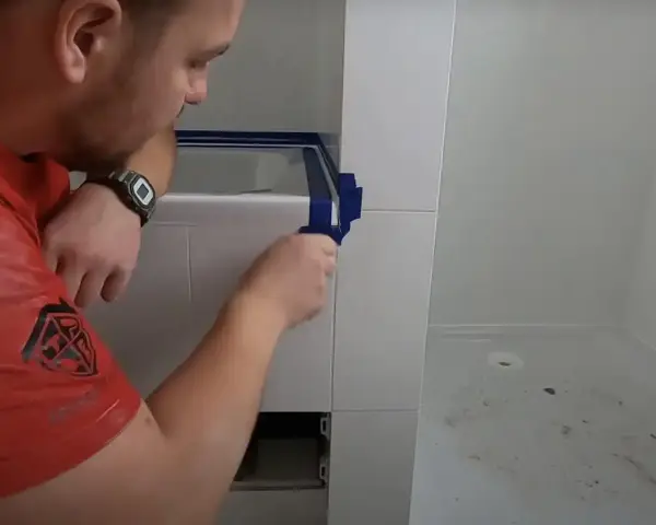 Mężczyzna okleja taśmą krawędzie płytek, przygotowując się do aplikacji fugi epoksydowej. Unikanie błędów to klucz do sukcesu.