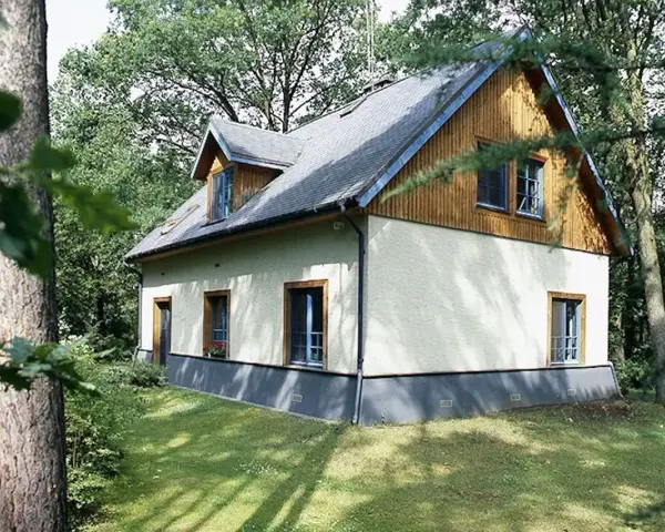 Dom otoczony zielenią, z widoczną odległością budynku od lasu. Drzewa tworzą naturalną barierę.