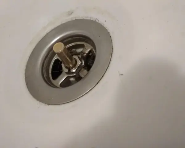 Metalowy korek do wanny z pokrętłem, widoczny mechanizm i włosy. Potrzebna naprawa.