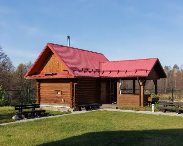 Drewniany domek letniskowy z czerwonym dachem, idealny na wypoczynek. Marzysz o takim? Sprawdź dofinansowanie na domek letniskowy!