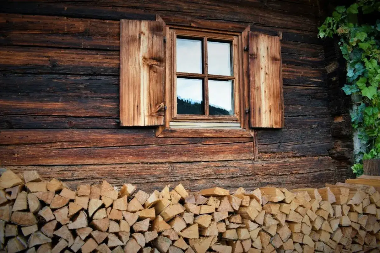 Drewniany dom w trakcie remontu. Okno z drewnianymi okiennicami, stos drewna opałowego.