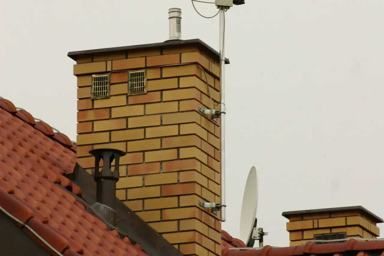 Komin z cegły z kratkami wentylacyjnymi, jak zrobić odpowietrzenie wc. Dachówki i antena satelitarna.