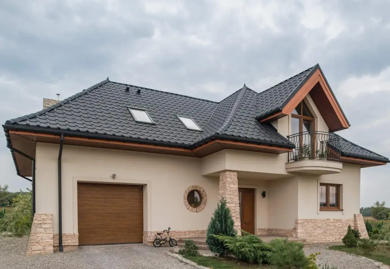 Nowoczesny dom z piaskowym kolorem elewacji, ciemnym dachem, garażem i balkonem.