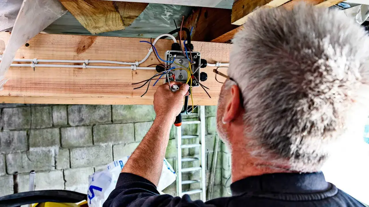 Elektryk kończy instalację elektryczną w garażu, łącząc przewody w puszce.