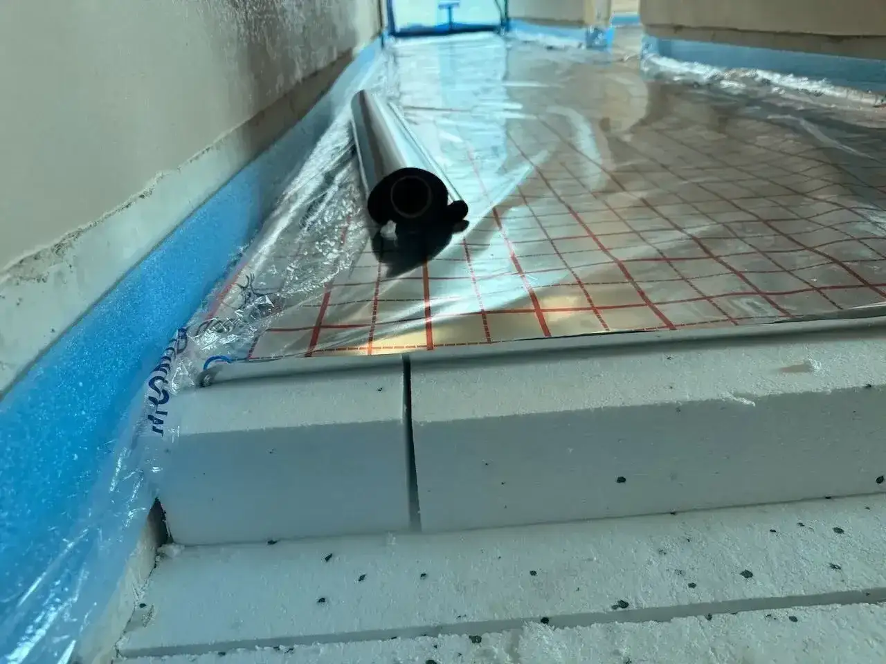 Układanie styropianu pod podłogówkę. Warstwa izolacyjna z folią aluminiową i taśmą brzegową.