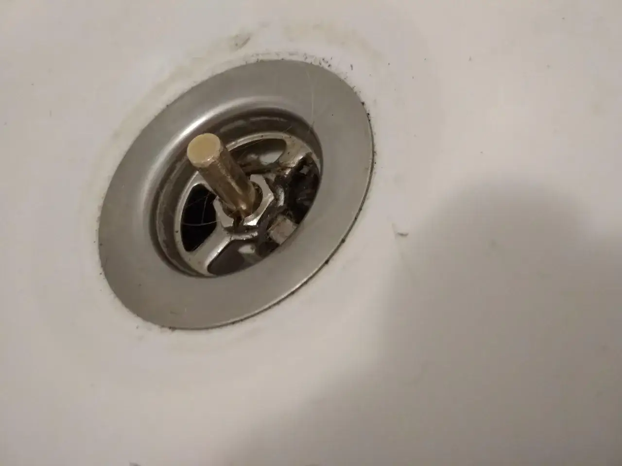 Metalowy korek do wanny z pokrętłem, widoczne włosy i brud. Potrzebna naprawa.