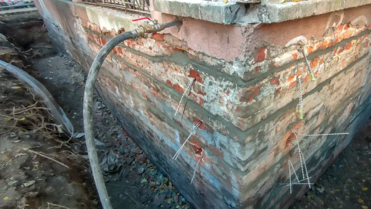 Naprawa pionowe pęknięcia ścian nośnych. Widać otwory i kotwy w ceglanej ścianie fundamentowej.