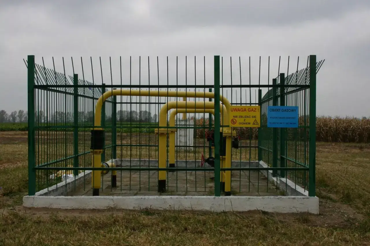 Ogrodzony obiekt gazowy z ż&oacute;łtymi rurami. Tablice ostrzegawcze informują o zagrożeniu. Odległość budynku od gazociągu średniego ciśnienia jest bezpieczna.