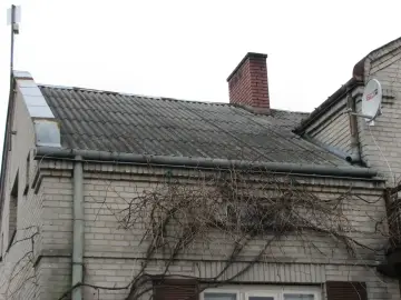 Dach pokryty eternitem, który zawiera azbest. Co to za materiał? Stary, szary eternit na dachu domu, z kominem i anteną satelitarną.